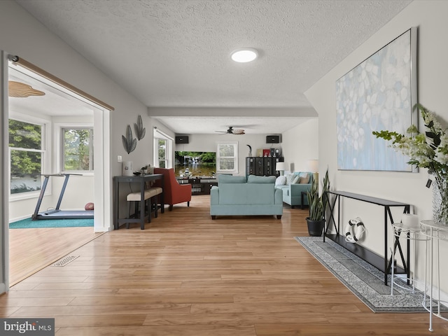 living area featuring a textured ceiling, ceiling fan, and light wood finished floors