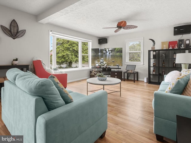 living area with healthy amount of natural light, ceiling fan, wood finished floors, a textured ceiling, and baseboards