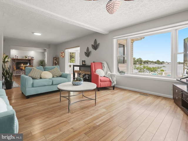 living area with a textured ceiling, ceiling fan, light wood-style floors, baseboards, and a brick fireplace
