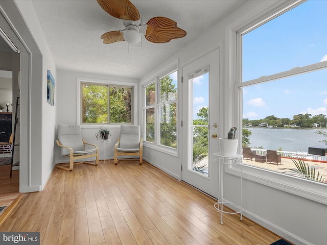 sunroom / solarium featuring a water view, wood finished floors, and baseboards