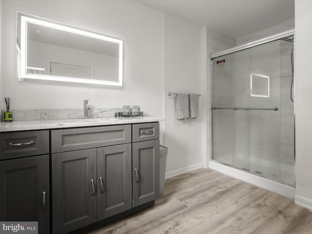 full bathroom featuring wood finished floors, a shower stall, vanity, and baseboards