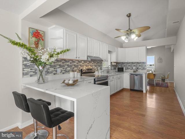 kitchen with stainless steel appliances, white cabinetry, tasteful backsplash, ceiling fan, and light stone counters