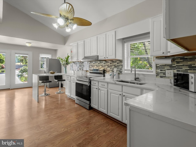kitchen featuring appliances with stainless steel finishes, a sink, vaulted ceiling, and white cabinets