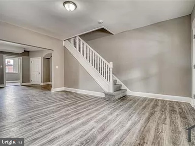 unfurnished living room featuring wood finished floors, baseboards, and stairs