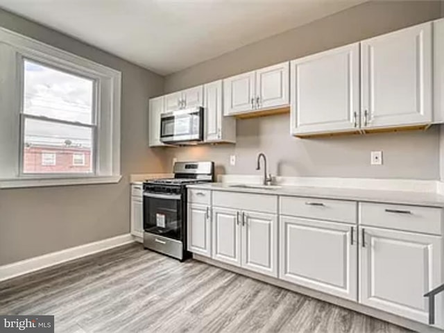 kitchen featuring stainless steel appliances, a sink, baseboards, and white cabinets