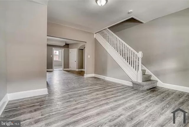 unfurnished living room featuring wood finished floors, baseboards, and stairway