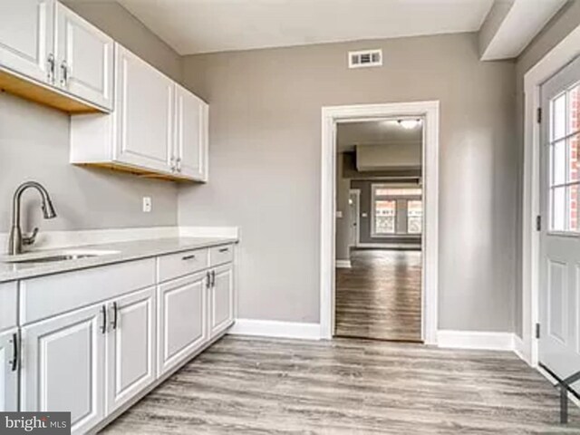 kitchen featuring a sink, light wood-style floors, baseboards, and white cabinets
