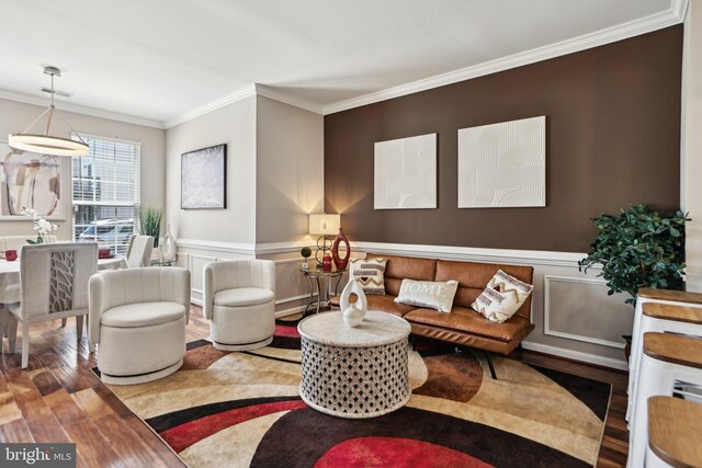 living room with wood finished floors, visible vents, a decorative wall, crown molding, and wainscoting