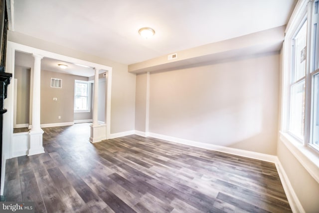 interior space featuring decorative columns, visible vents, baseboards, and dark wood finished floors