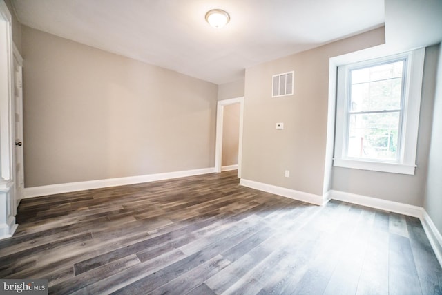 unfurnished room featuring dark wood-type flooring, visible vents, and baseboards