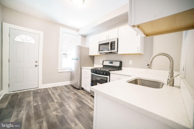 kitchen with dark wood-style flooring, baseboards, white cabinets, appliances with stainless steel finishes, and a sink