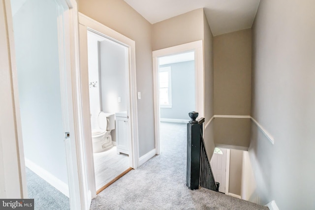 hall featuring carpet floors, baseboards, and an upstairs landing