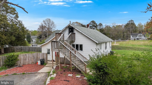 view of front facade with fence, a front lawn, stairway, and roof with shingles