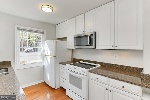 kitchen featuring light wood-style flooring, dark stone counters, baseboards, white cabinetry, and white appliances