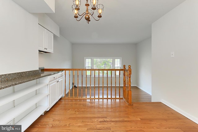 hallway featuring baseboards, a chandelier, and light wood-style floors