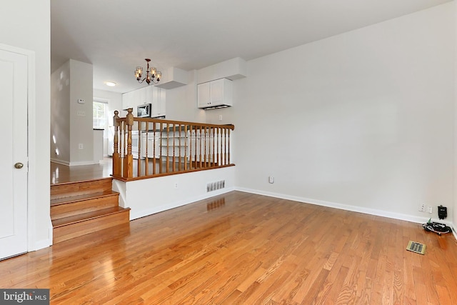 spare room with baseboards, visible vents, a chandelier, and light wood finished floors