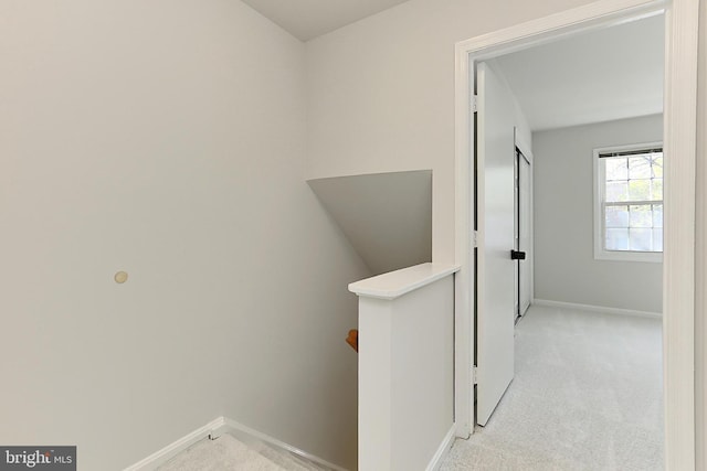 hallway featuring light colored carpet, baseboards, and an upstairs landing