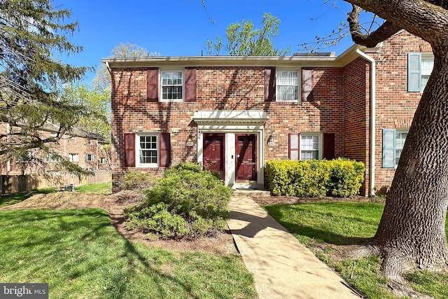 colonial inspired home featuring brick siding and a front yard
