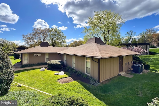 exterior space with a yard, central air condition unit, and roof with shingles