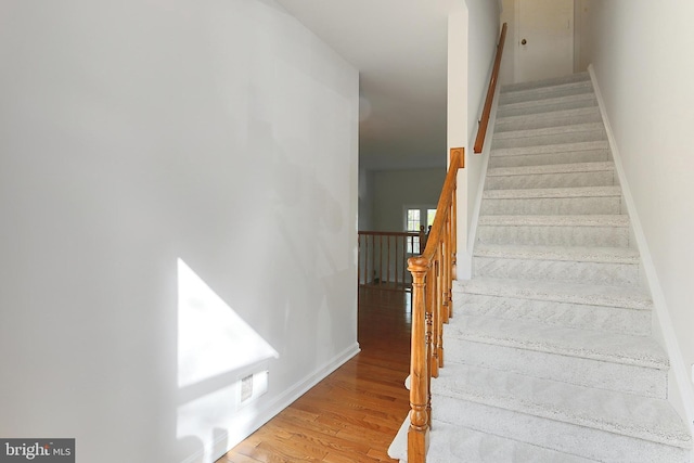 staircase with wood finished floors, visible vents, and baseboards