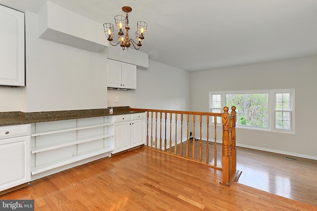 interior space featuring light wood-style flooring, visible vents, baseboards, and an inviting chandelier