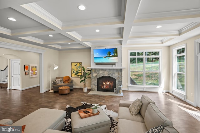 living area featuring coffered ceiling, ornamental molding, wood finished floors, and a stone fireplace
