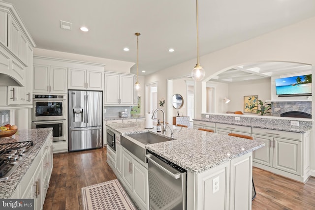 kitchen with recessed lighting, stainless steel appliances, a sink, arched walkways, and a center island with sink