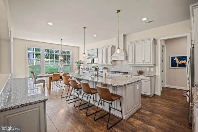 kitchen with visible vents, dark wood-type flooring, appliances with stainless steel finishes, and premium range hood