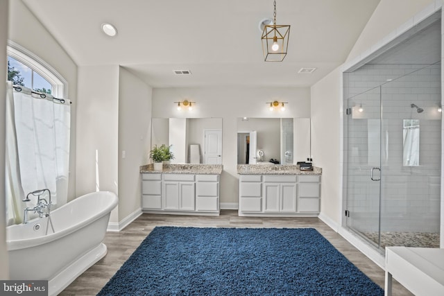 full bath featuring a shower stall, wood finished floors, a sink, two vanities, and visible vents