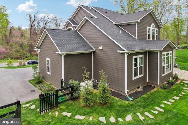 view of home's exterior featuring roof with shingles, fence, and a lawn