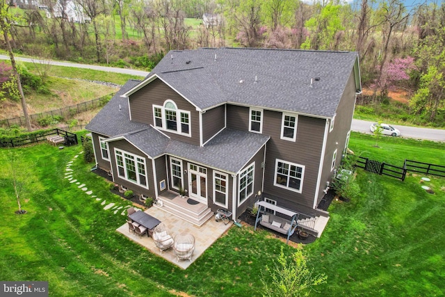 back of property with fence, a wooden deck, a shingled roof, a yard, and a patio