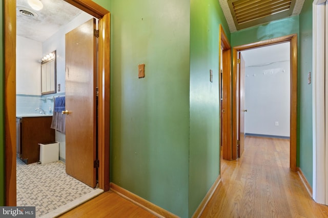 hallway featuring light wood-style floors, visible vents, baseboards, and a sink
