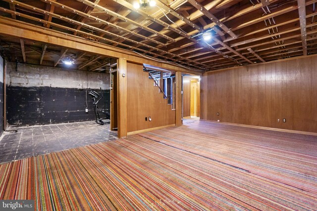 finished basement with wooden walls, carpet floors, and stairway