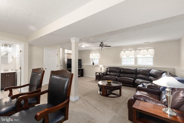 living room with ceiling fan, light carpet, a textured ceiling, baseboards, and decorative columns