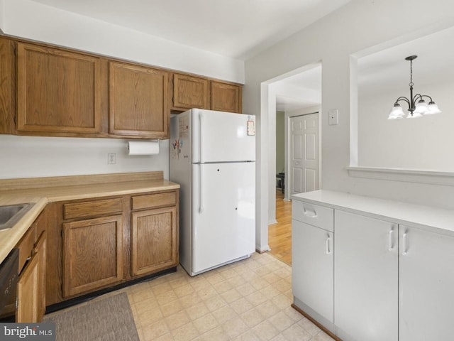 kitchen featuring light countertops, a chandelier, brown cabinetry, freestanding refrigerator, and light floors