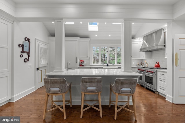 6068 Stoney Hill Rd, New Hope, PA 18938 - kitchen with range with two ovens, wall chimney range hood, a sink, decorative columns, and a breakfast bar area