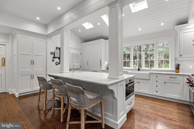 6068 Stoney Hill Rd, New Hope, PA 18938 - kitchen with white cabinets, a sink, lofted ceiling with skylight, dark wood-style flooring, and decorative columns