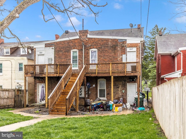 rear view of house featuring brick siding, a wooden deck, a yard, and fence