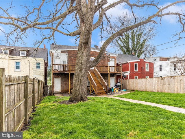 back of property with stairs, brick siding, a deck, a fenced backyard, and a lawn