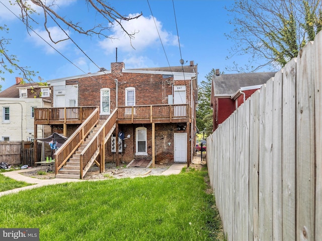 rear view of house with a wooden deck, a fenced backyard, brick siding, stairs, and a lawn