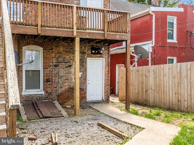 doorway to property featuring brick siding, fence, and a wooden deck
