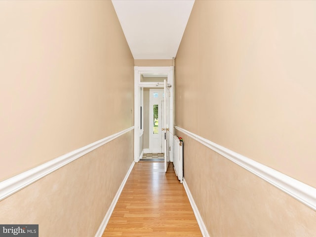 corridor with baseboards, light wood-style flooring, and radiator heating unit