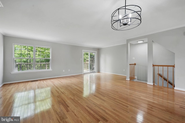 unfurnished living room featuring light wood-style floors, ornamental molding, a chandelier, and baseboards