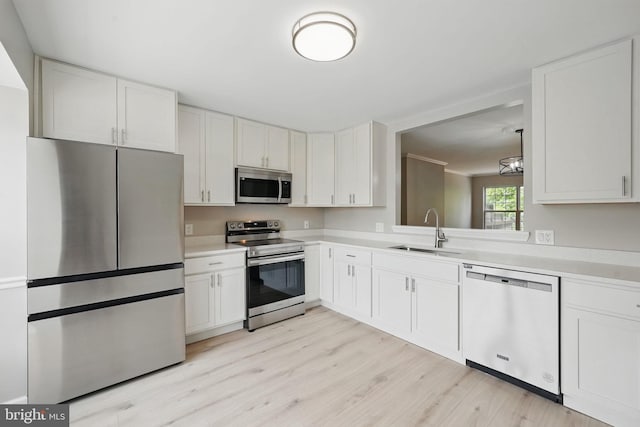 kitchen with stainless steel appliances, a sink, light wood-style floors, light countertops, and white cabinetry