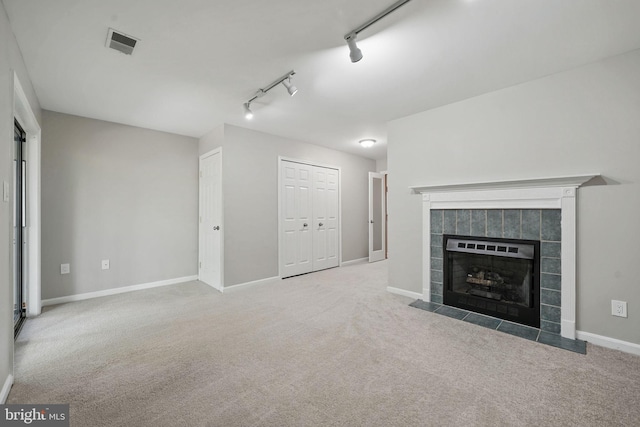 unfurnished living room with rail lighting, carpet, a tiled fireplace, and baseboards