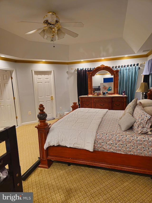 bedroom with a raised ceiling, light colored carpet, and a ceiling fan