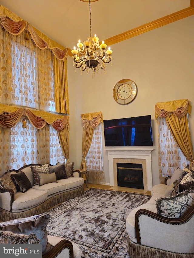 living area with a chandelier, a fireplace with flush hearth, a towering ceiling, and ornamental molding