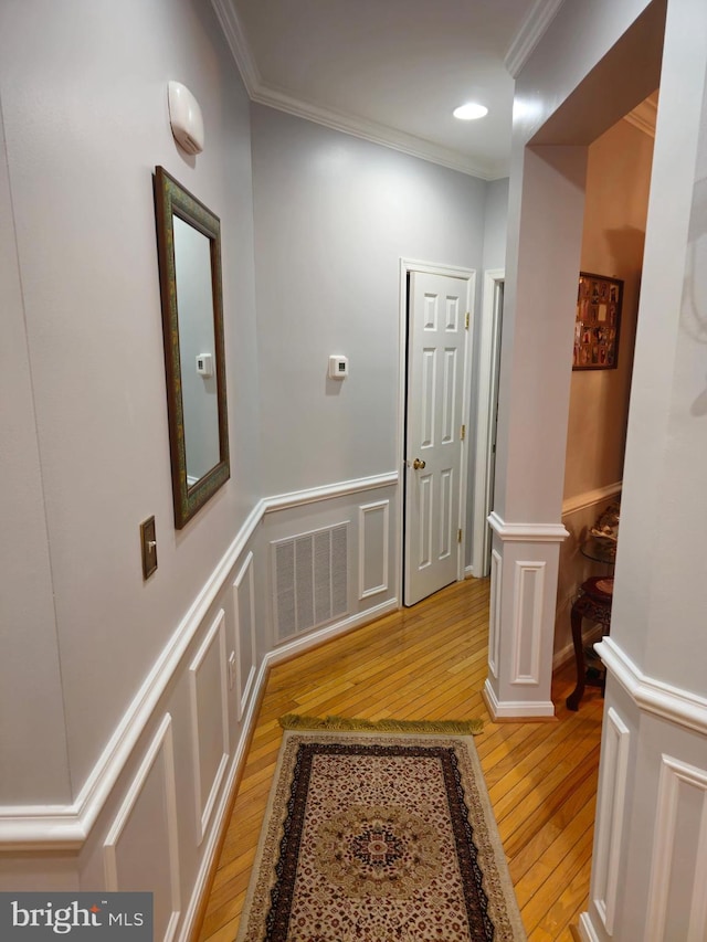 hallway featuring crown molding, visible vents, a wainscoted wall, and light wood-type flooring