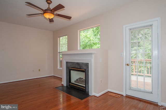 unfurnished living room featuring ceiling fan, visible vents, a fireplace with flush hearth, baseboards, and wood-type flooring