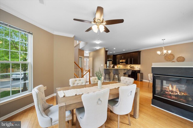 dining room featuring a chandelier, stairway, light wood-style flooring, ceiling fan, and crown molding